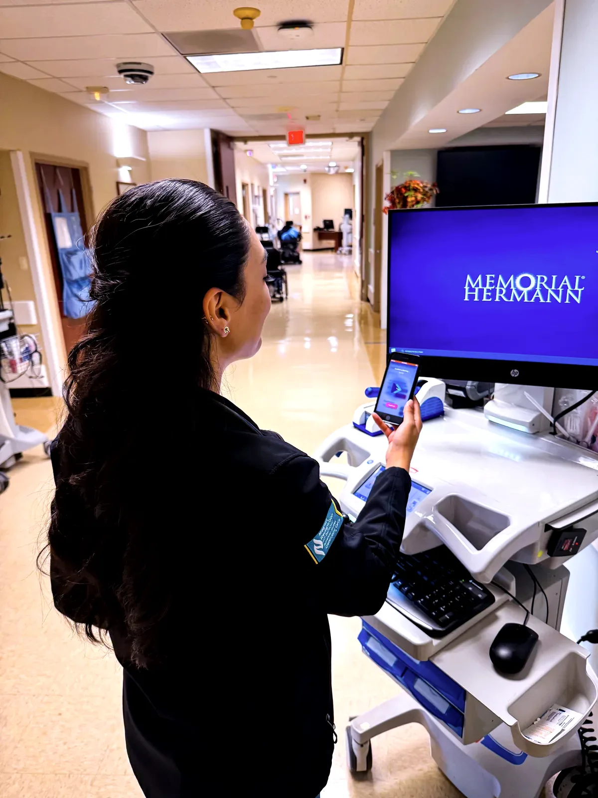 A nurse at a workstation on wheels in the corridor, using CareShift on her phone
